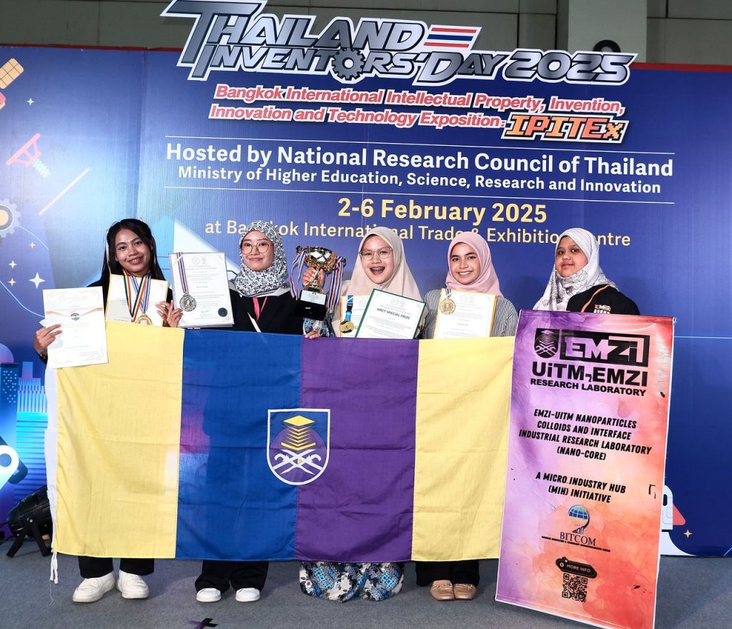 IPITEx 2025: Team with the UiTM flag and the NANO-CORE banner at the Thailand Inventors’ Day 2025 backdrop